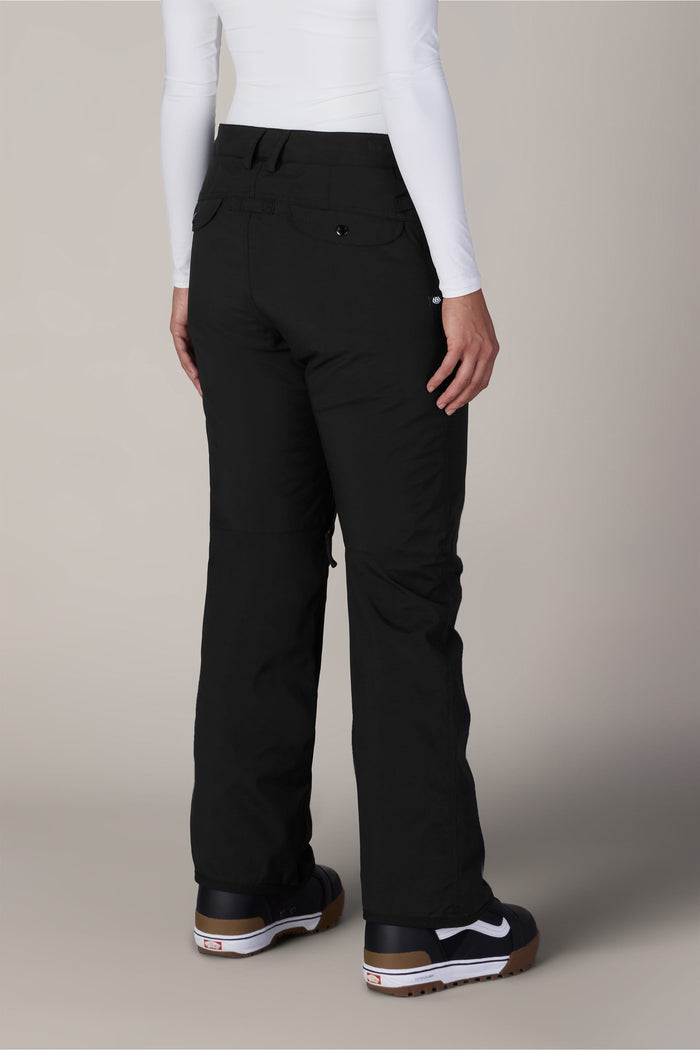 A person wearing the 686 Womenβs Standard Shell Pant by 686, paired with a white long-sleeve shirt and black sneakers with white soles, is standing with their back to the camera against a plain background.