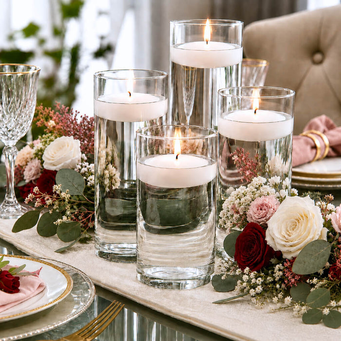 Centerpiece with four floating candles in glass vases, flowers, and greenery on a table