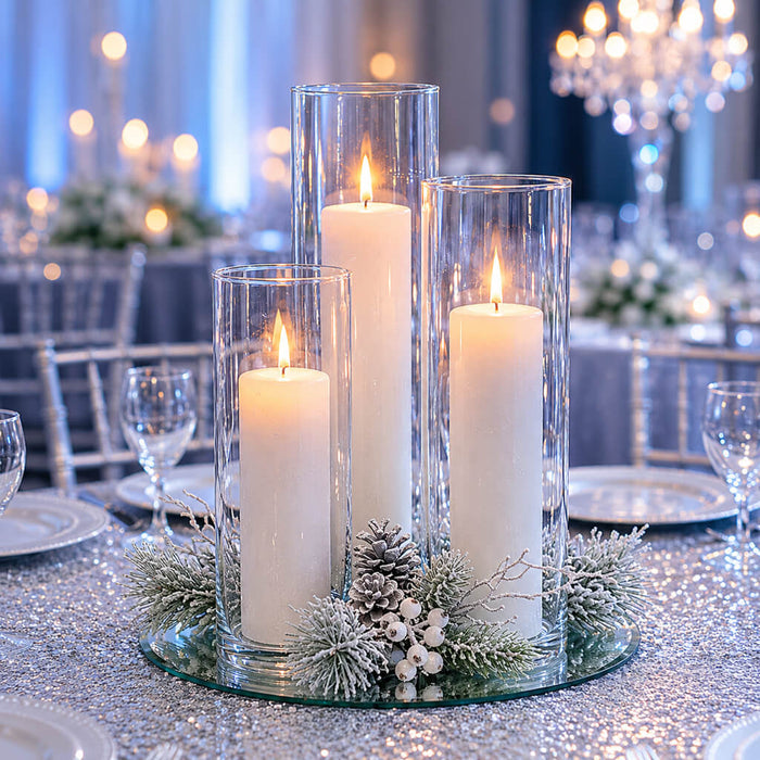 Three lit candles in glass vases with winter greenery on a glitter tabletop