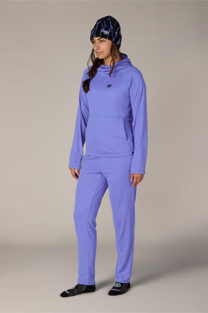 A person stands against a plain light background, looking slightly to the side, dressed in a matching light purple set and a patterned beanie with black socks. The cozy ensemble calls to mind the 686 Women’s Mission Grid™ Hoody by 686—soft, comfortable, and ideal for casual style.
