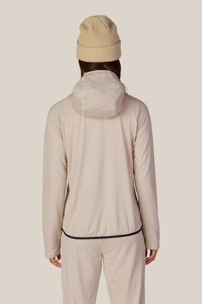 A person facing away, wearing a beige beanie and the 686 Women’s Mission Grid™ Hoody by 686 in a light checkered pattern, paired with matching pants, against a plain light background.