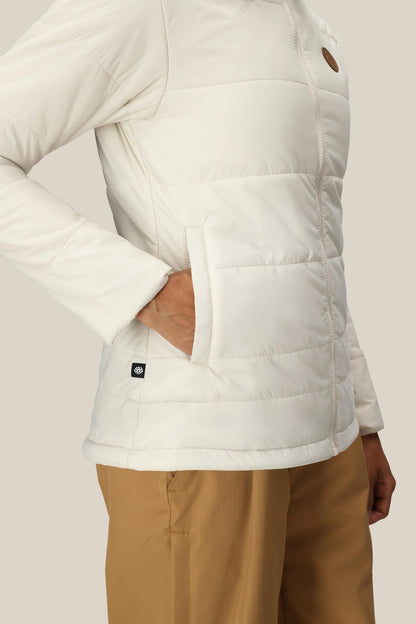 A woman wearing the 686 Women’s Thermal Puff Insulated Jacket with one hand in the pocket and tan pants stands against a neutral background.