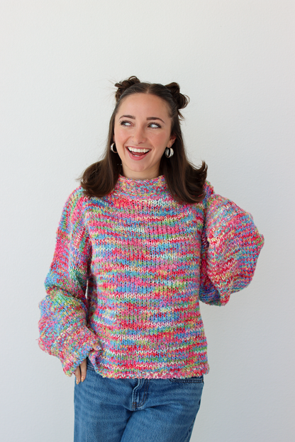 Woman wearing a pink multicolor crochet knit mock neck sweater with blue denim jeans