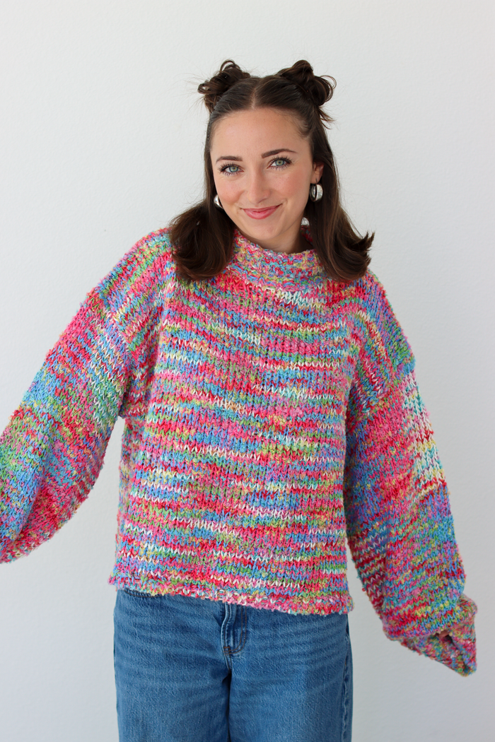 Woman wearing a pink multicolor crochet knit mock neck sweater with blue denim jeans