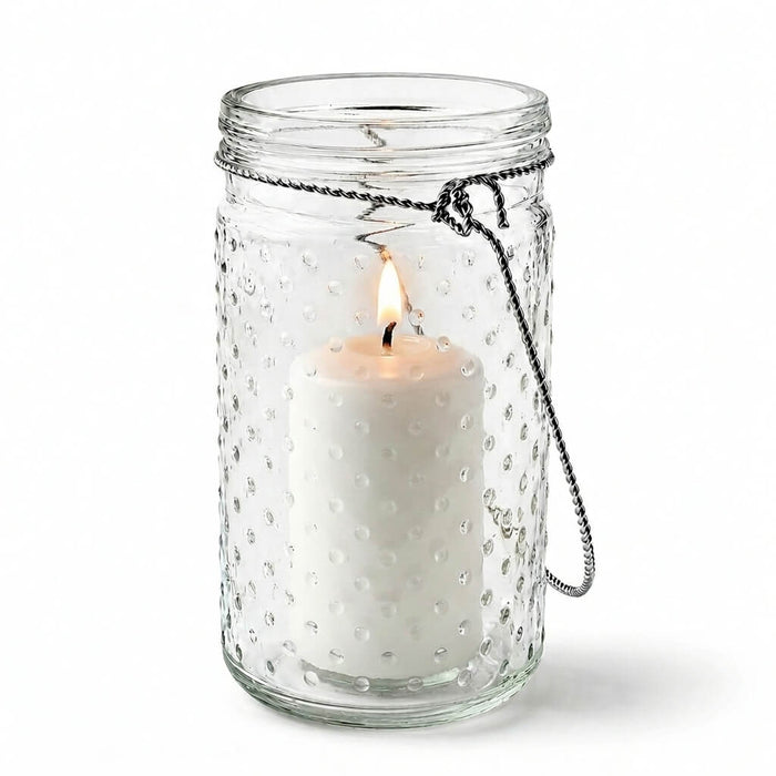 7.5 inch hanging dotted glass jar with handle and a lit pillar candle inside