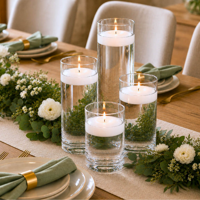 Centerpiece with four floating candles in glass vases, greenery, and white flowers on a table