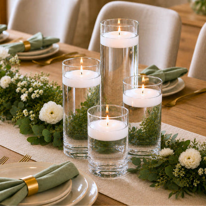 Centerpiece with four floating candles in glass vases, greenery, and white flowers on a table