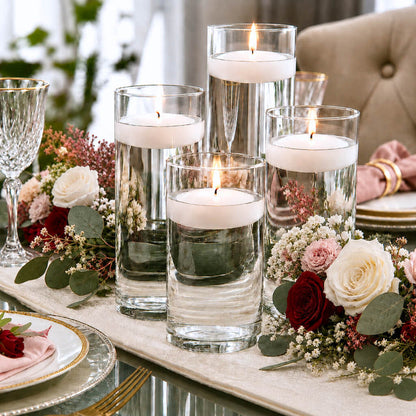 Centerpiece with four floating candles in glass vases, flowers, and greenery on a table