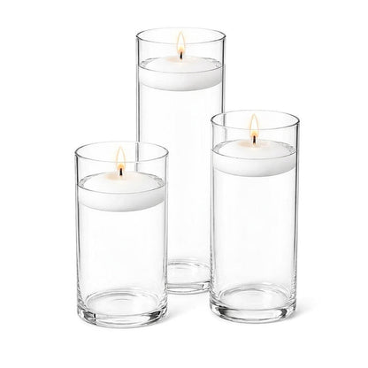 Three lit white floating candles in cylindrical glass vases filled with water