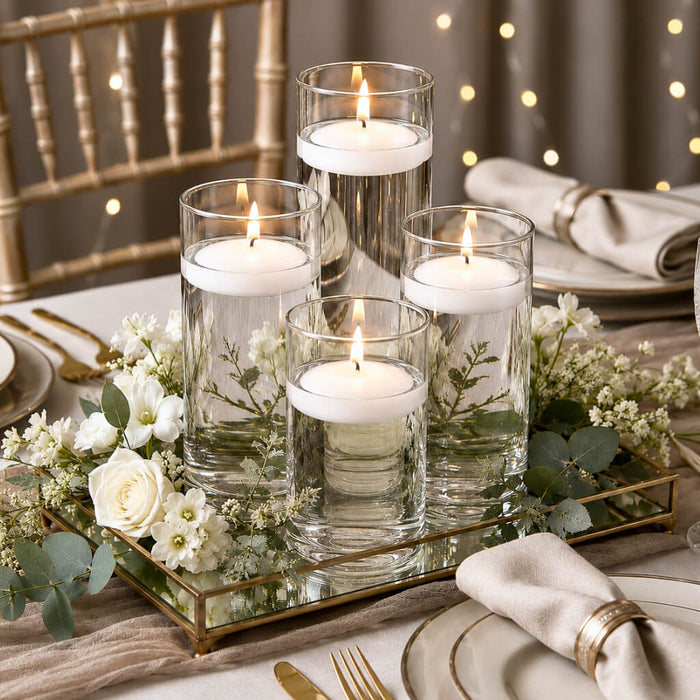 Centerpiece with four burning floating candles in glass vases, white roses, and greenery