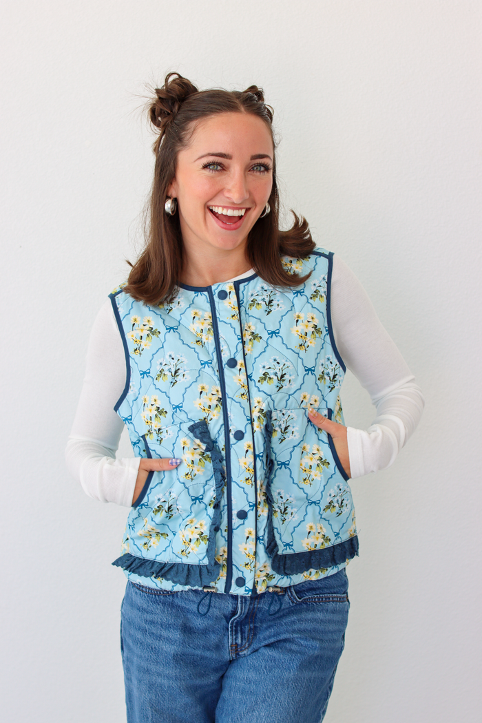 Woman wearing a blue floral puffer vest with a white long sleeve shirt and blue denim jeans
