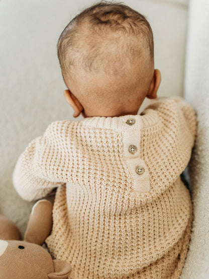 Baby wearing beige Viverano Organics baby top made from organic cotton with button details on back
