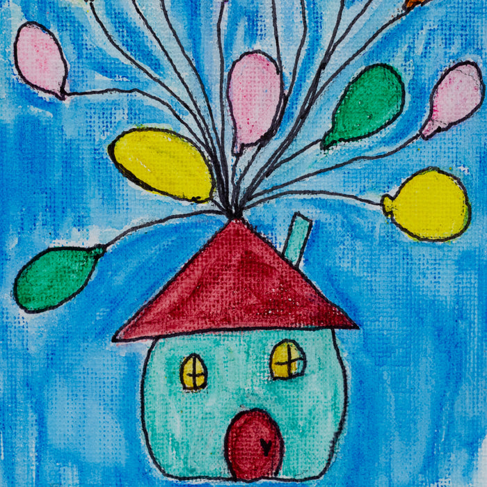 A colorful canvas painting featuring a house with a red roof and multiple balloons in various colors released from the top of the house, set against a blue background. The painting is displayed on a small easel.
