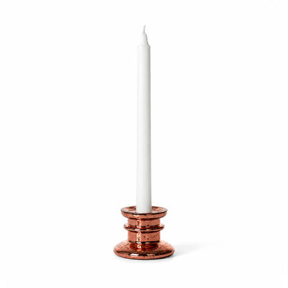 A rose gold taper candle holder with a white taper candle