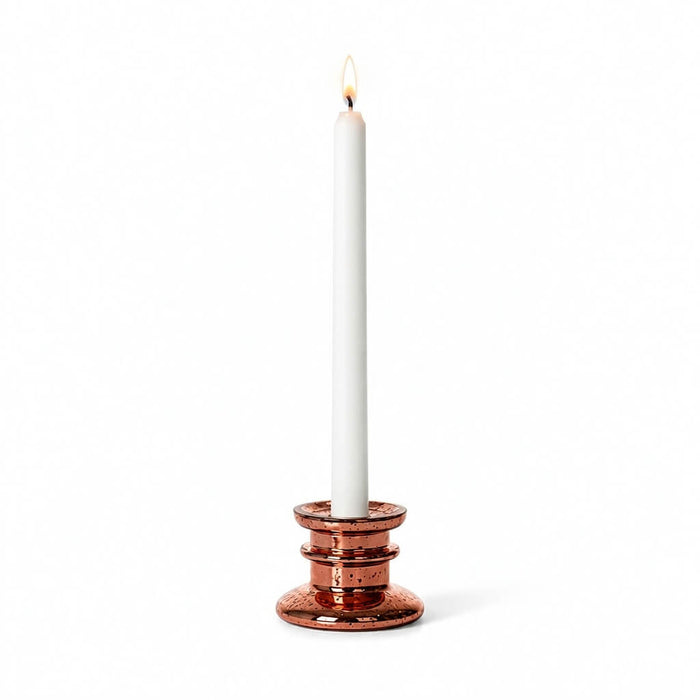 A rose gold taper candle holder with a lit white candle