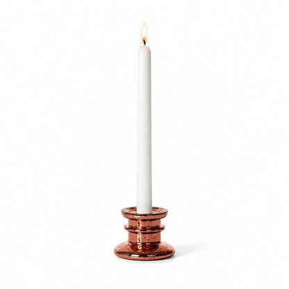 A rose gold taper candle holder with a lit white candle