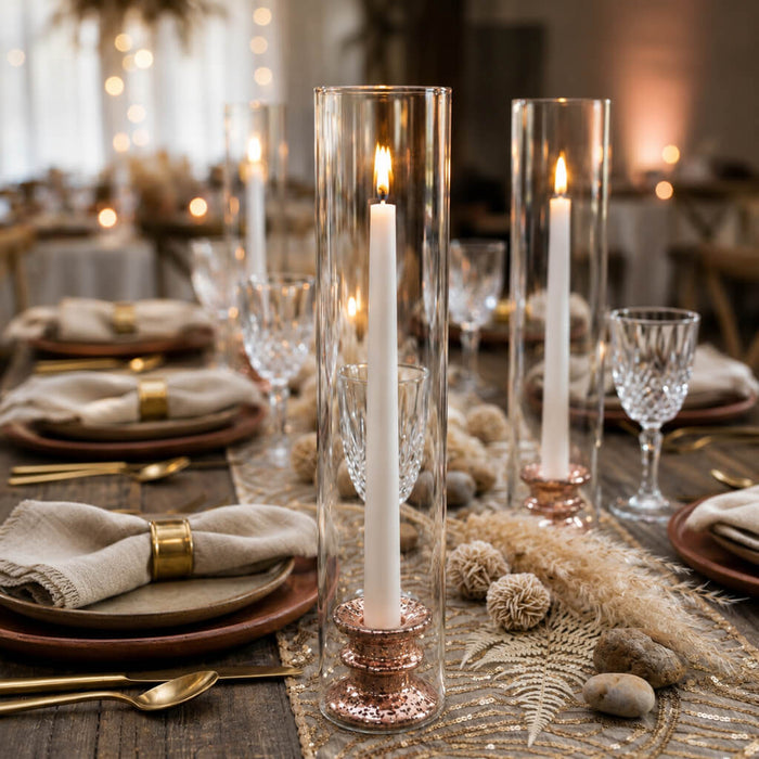 Rose gold taper candle holders inside glass cylinders on a decorated dining table