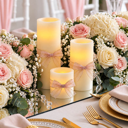 Ivory flameless LED pillar candles decorated with bows, surrounded by pink and white flowers