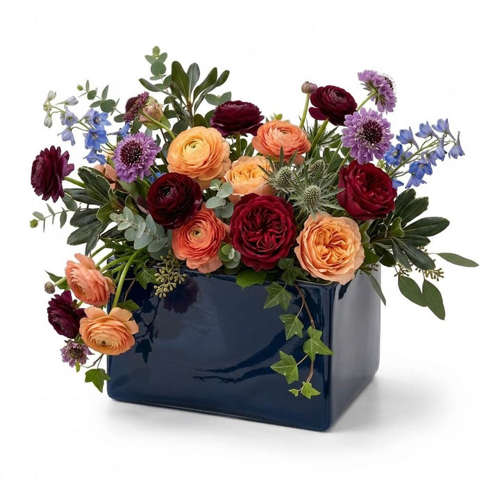 Navy blue square vase overflowing with a rich, colorful bouquet of autumn-toned flowers