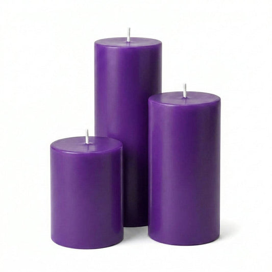 Three unlit purple pillar candles in assorted sizes on a solid white background