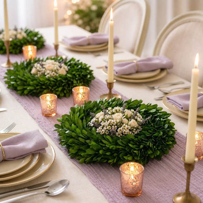 Preserved boxwood wreaths with flowers set as table centerpieces with candles on a lilac runner
