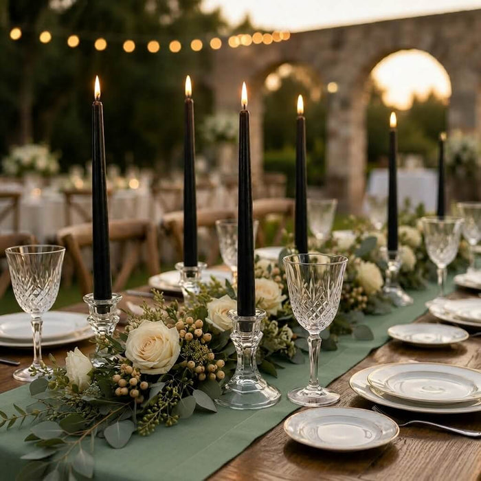 Lit black taper candles on outdoor dining table with floral garland
