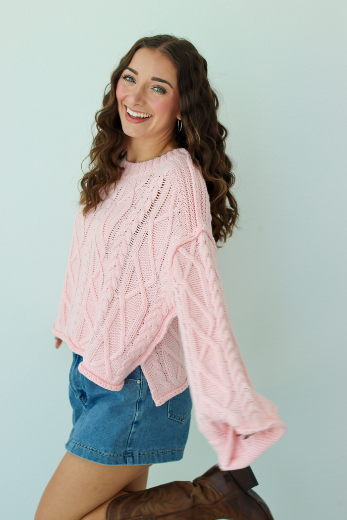 Woman wearing a pink knit sweater with a blue denim mini skirt and brown boots