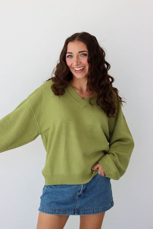 Woman wearing a v-neck green sweater with a blue denim mini skirt