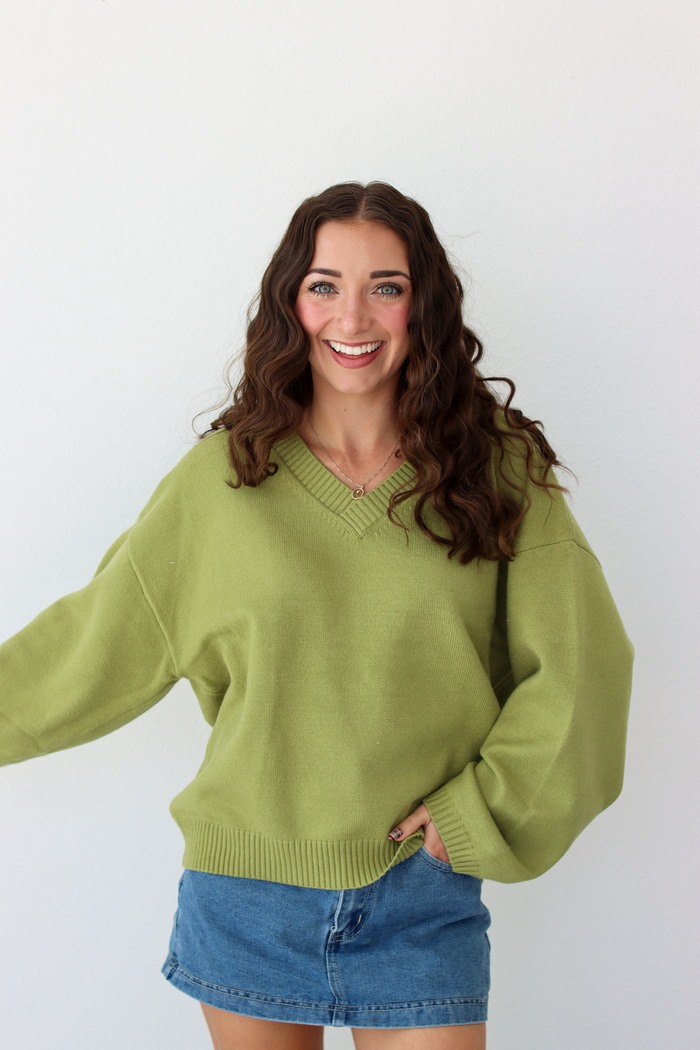 Woman wearing a v-neck green sweater with a blue denim mini skirt