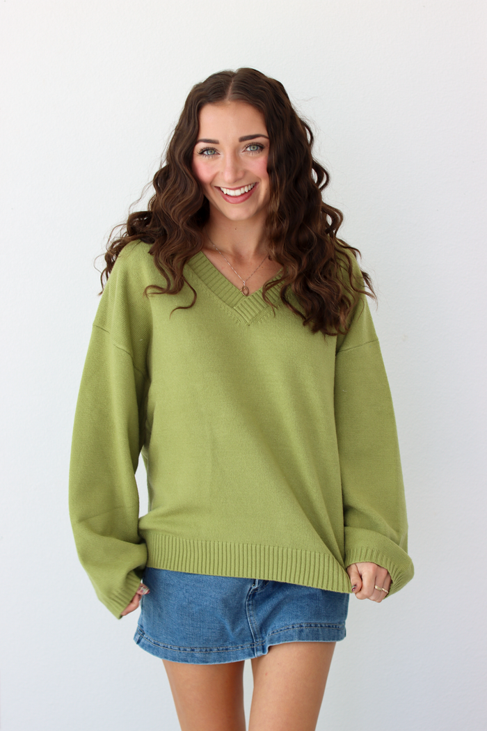 Woman wearing a v-neck green sweater with a blue denim mini skirt