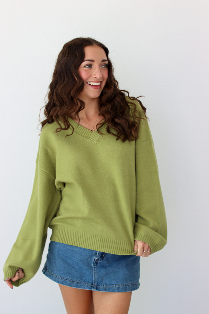 Woman wearing a v-neck green sweater with a blue denim mini skirt